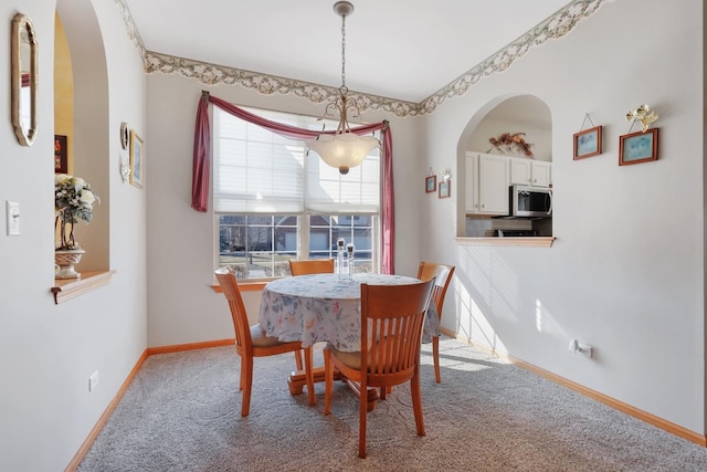 dining space with baseboards, carpet, and arched walkways