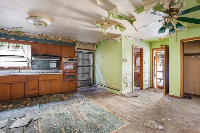 kitchen with a sink, cooktop, light countertops, under cabinet range hood, and brown cabinets