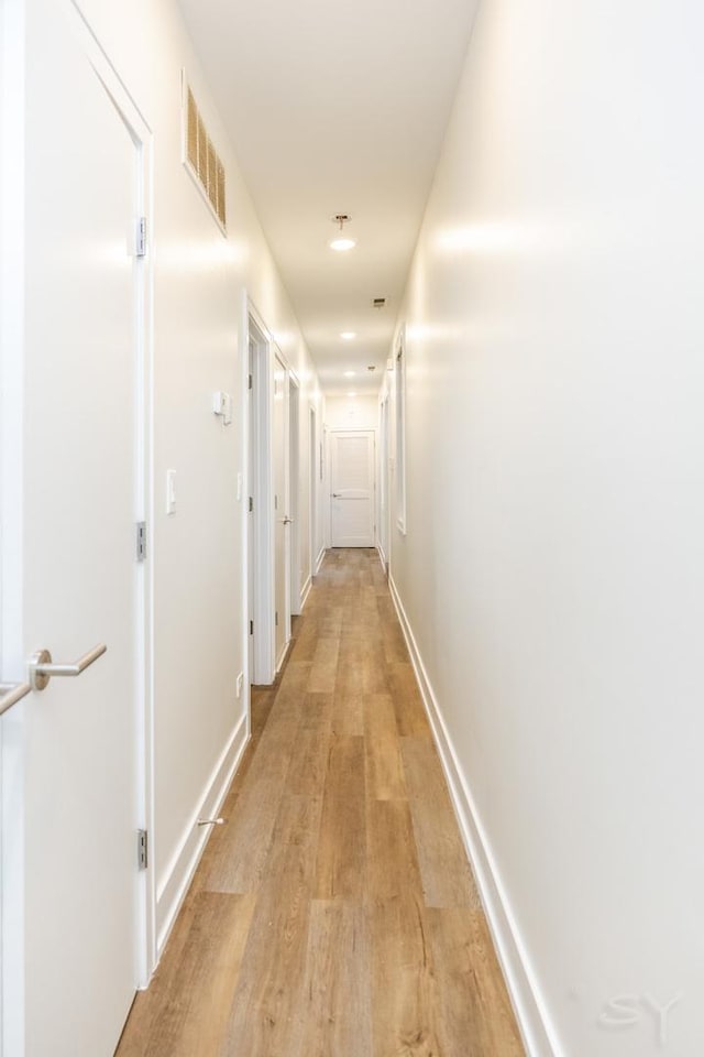 hall featuring visible vents, baseboards, and light wood-style floors