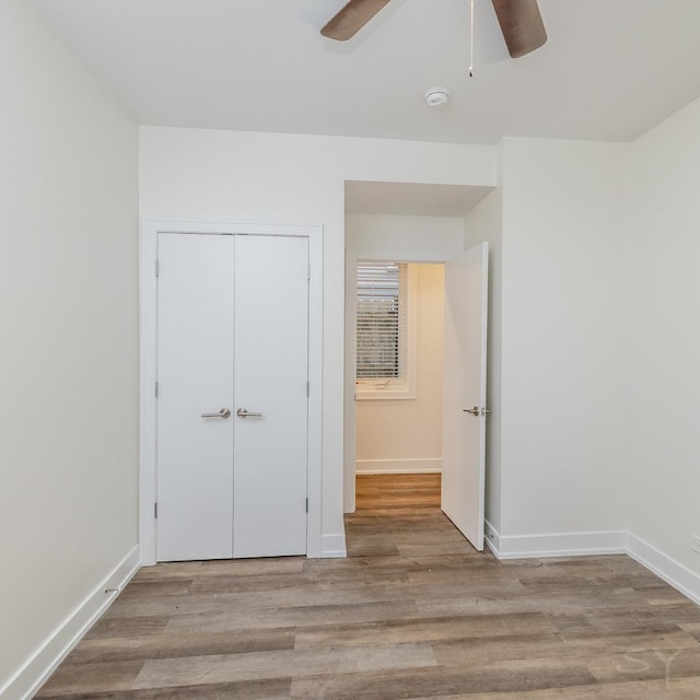 unfurnished bedroom with a closet, baseboards, wood finished floors, and a ceiling fan