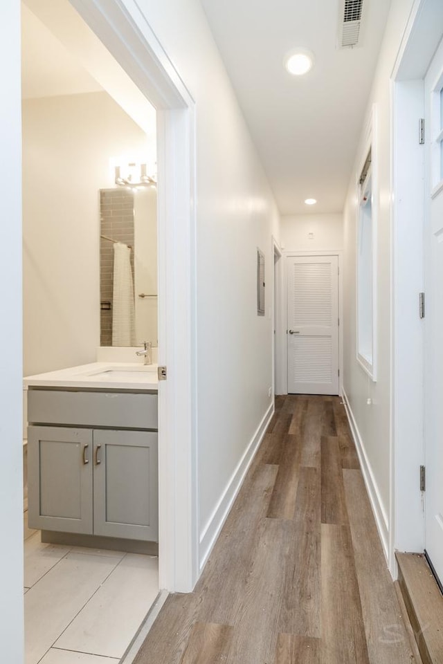 corridor with a sink, light wood-style floors, visible vents, and baseboards