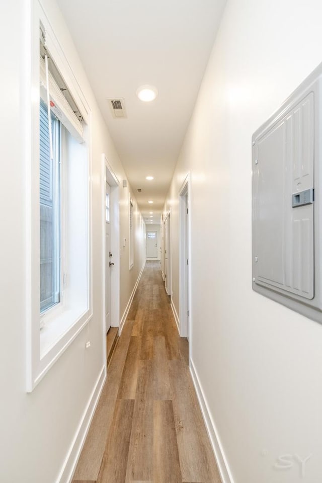 corridor featuring electric panel, visible vents, light wood-style flooring, and baseboards