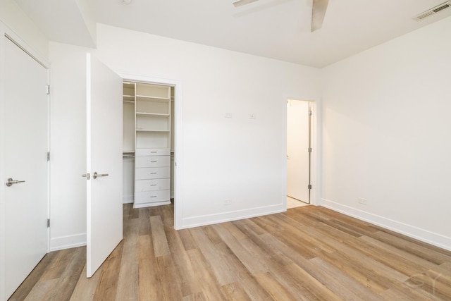 unfurnished bedroom featuring visible vents, baseboards, a walk in closet, and light wood finished floors