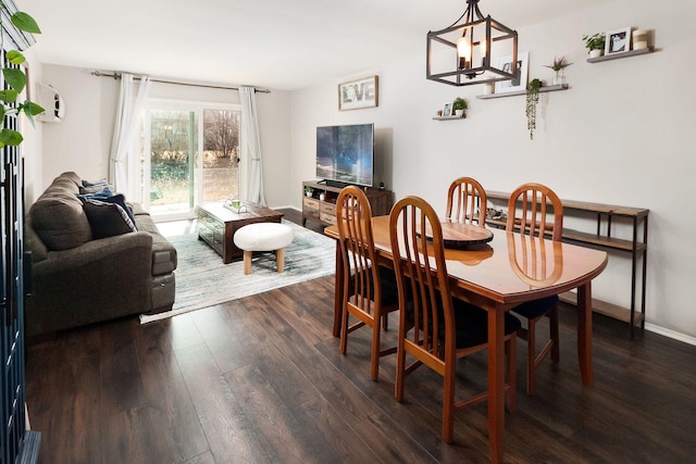 dining area with dark wood-type flooring, a notable chandelier, and baseboards