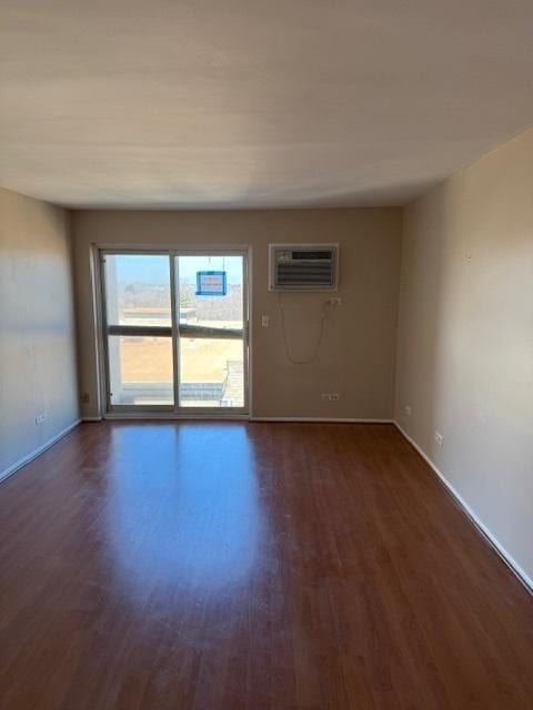 empty room with dark wood-style floors, baseboards, and a wall mounted air conditioner