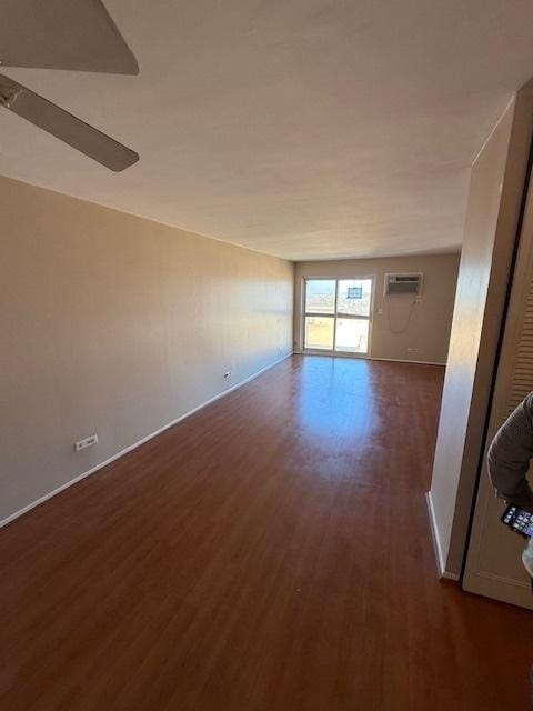 empty room with a wall mounted air conditioner, baseboards, and dark wood-style floors