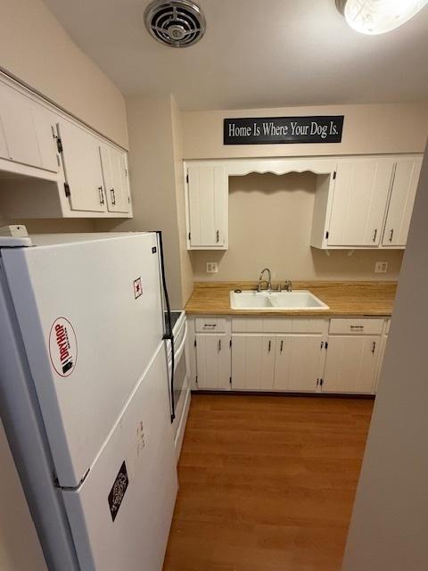 kitchen with a sink, visible vents, white cabinetry, and freestanding refrigerator