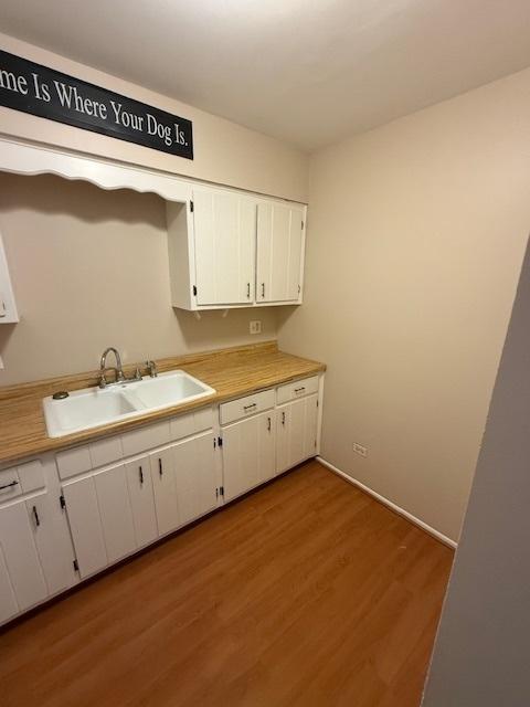 kitchen featuring a sink, wood finished floors, light countertops, and white cabinetry