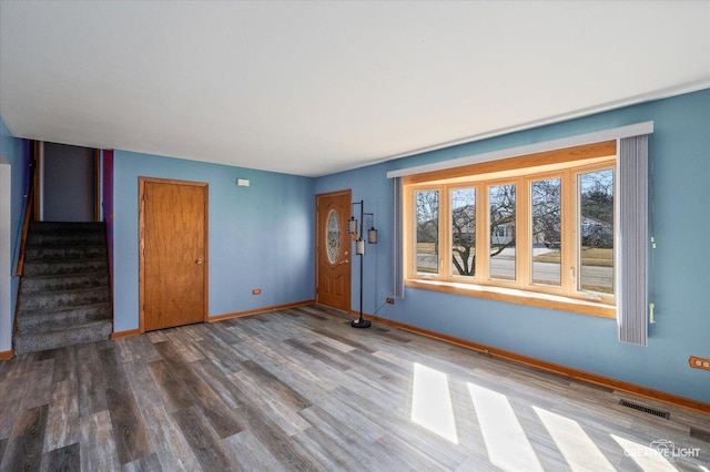 unfurnished living room with visible vents, stairway, baseboards, and wood finished floors