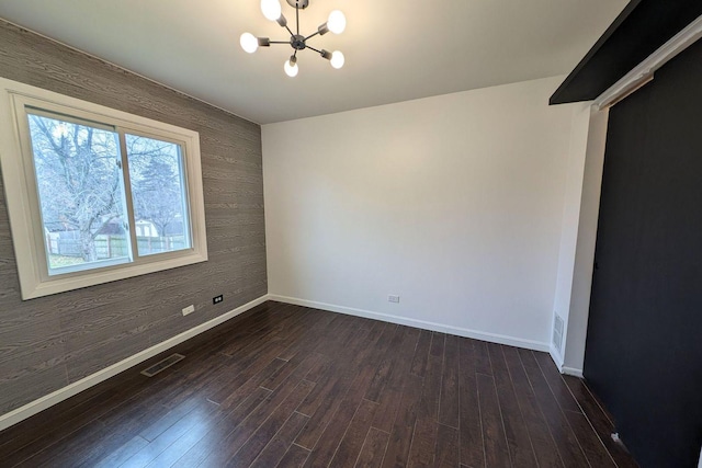 unfurnished room with visible vents, baseboards, a notable chandelier, and dark wood finished floors