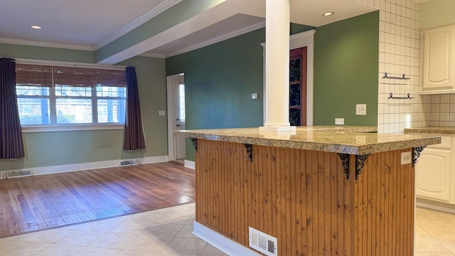 kitchen featuring crown molding, a kitchen breakfast bar, visible vents, and tile countertops