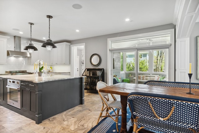 kitchen with white cabinetry, stainless steel appliances, wall chimney range hood, and a kitchen island with sink