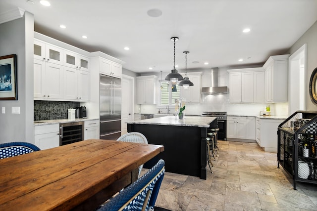 kitchen with a kitchen island, white cabinets, wine cooler, wall chimney range hood, and premium appliances