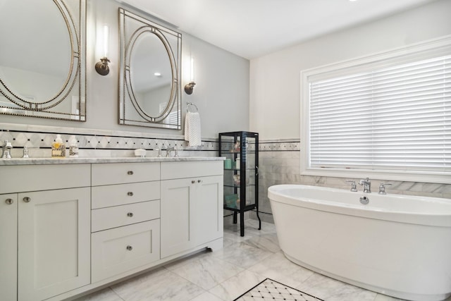 bathroom featuring a wainscoted wall, a soaking tub, double vanity, tile walls, and marble finish floor