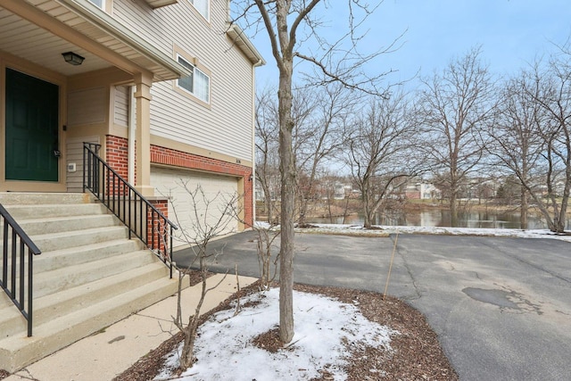 view of snow covered exterior with brick siding, concrete driveway, an attached garage, and entry steps