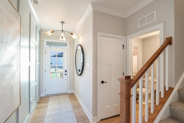 foyer with light wood finished floors, visible vents, baseboards, stairs, and ornamental molding