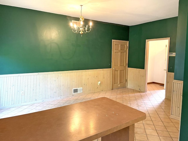 unfurnished dining area featuring tile patterned floors, visible vents, a notable chandelier, and a wainscoted wall