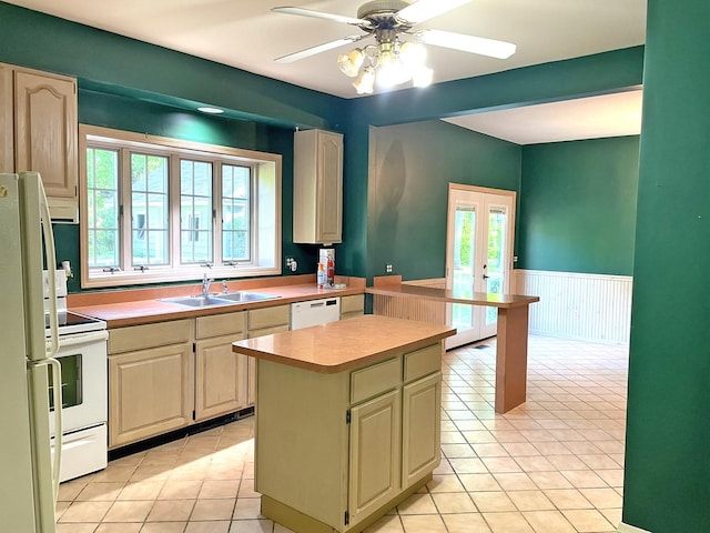 kitchen featuring white appliances, a wainscoted wall, a kitchen island, a sink, and light countertops