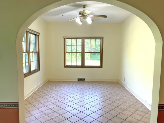 empty room with visible vents, arched walkways, light tile patterned flooring, baseboards, and ceiling fan