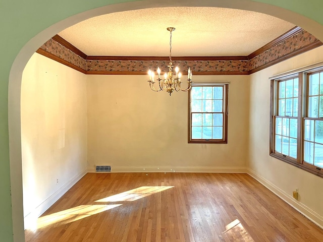 spare room with visible vents, arched walkways, wood-type flooring, a textured ceiling, and crown molding