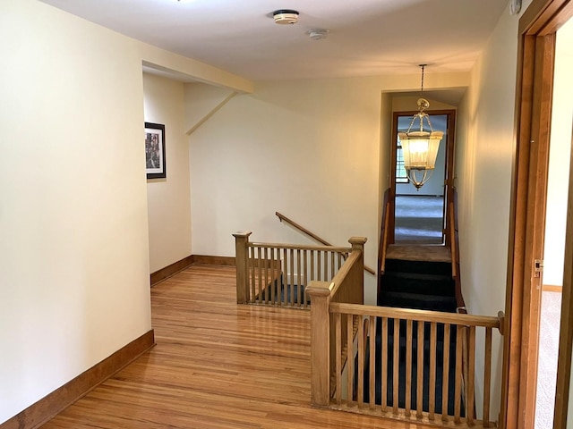 corridor with baseboards, an upstairs landing, and wood finished floors