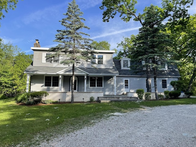 view of front of house featuring brick siding, covered porch, a chimney, and a front lawn