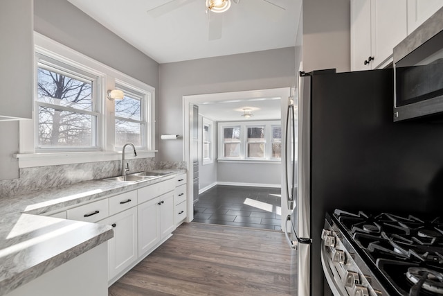 kitchen with a sink, ceiling fan, appliances with stainless steel finishes, white cabinetry, and dark wood-style flooring