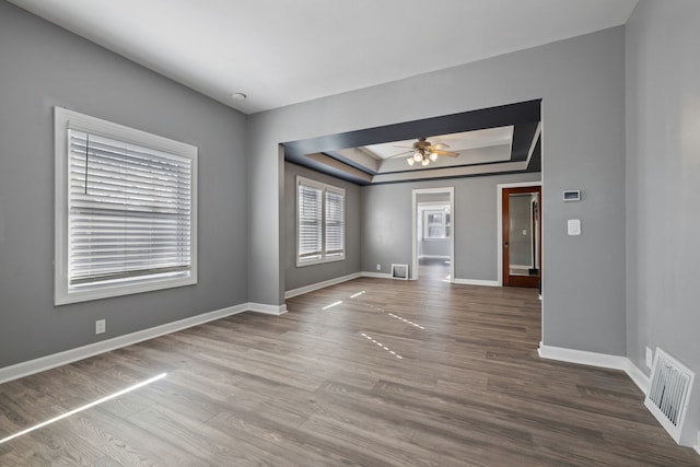 unfurnished room with visible vents, a ceiling fan, a tray ceiling, wood finished floors, and baseboards