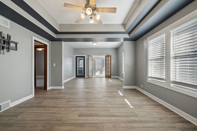 empty room featuring a ceiling fan, wood finished floors, baseboards, visible vents, and a tray ceiling