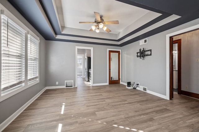 empty room with a tray ceiling, light wood-style floors, visible vents, and baseboards