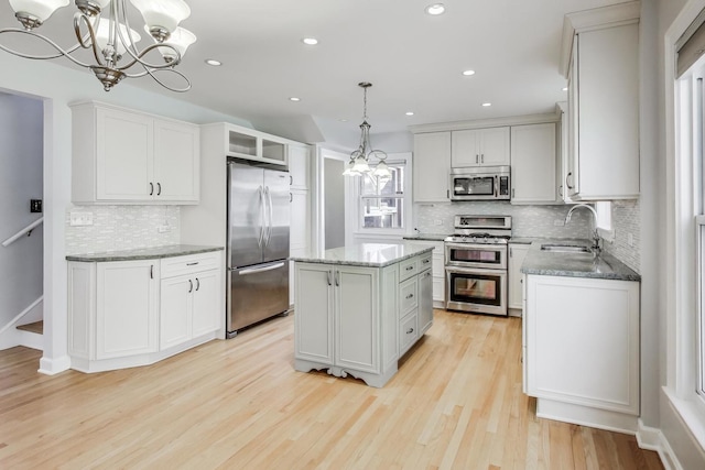 kitchen with a sink, stainless steel appliances, light stone counters, and a chandelier