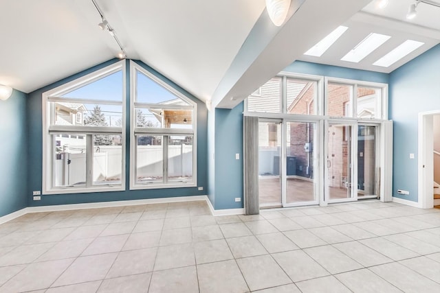 tiled empty room with lofted ceiling with skylight, baseboards, and track lighting