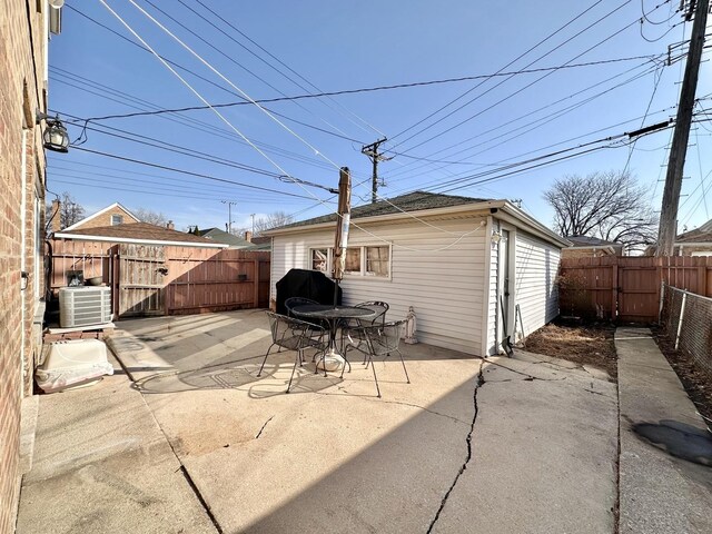 view of patio with grilling area, central air condition unit, a fenced backyard, an outbuilding, and a gate