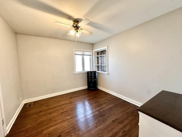 empty room featuring visible vents, baseboards, dark wood finished floors, and a ceiling fan