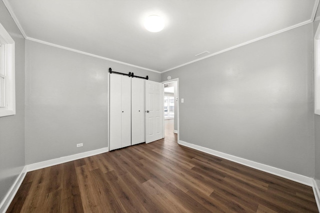 unfurnished bedroom with a barn door, baseboards, dark wood-type flooring, and crown molding