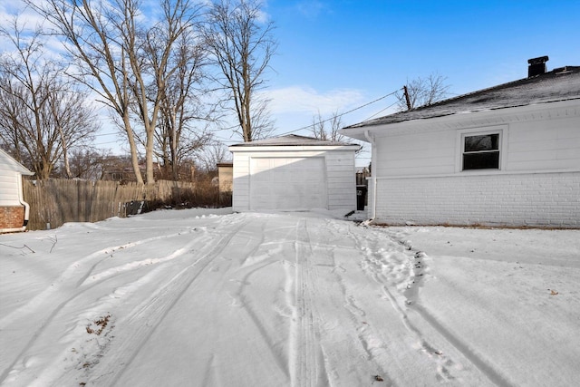 yard layered in snow with an outbuilding, fence, and a garage