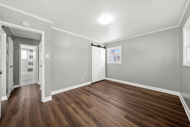 unfurnished bedroom with a barn door, baseboards, dark wood-type flooring, and ornamental molding