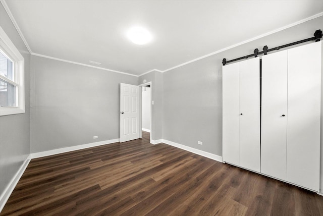 unfurnished bedroom with a barn door, baseboards, dark wood-type flooring, and crown molding