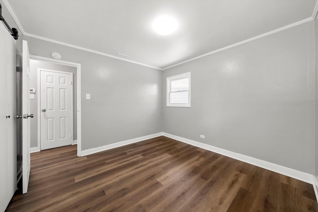 spare room with a barn door, baseboards, ornamental molding, and dark wood finished floors