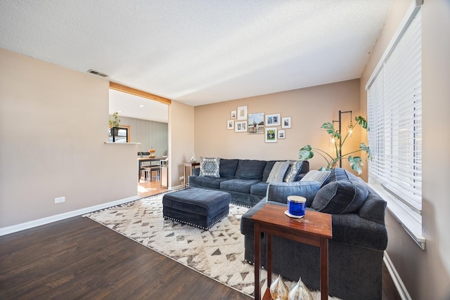 living area with a wealth of natural light, visible vents, a textured ceiling, and wood finished floors