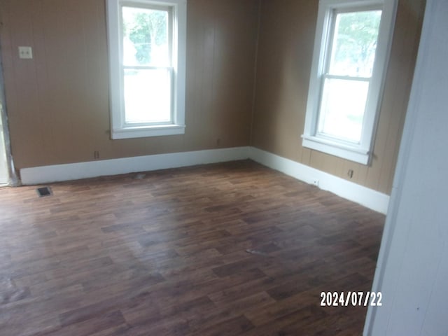 spare room with visible vents, plenty of natural light, dark wood-type flooring, and baseboards