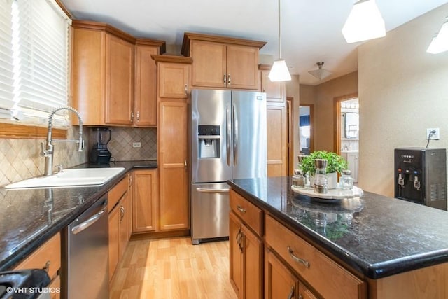 kitchen with a sink, backsplash, stainless steel appliances, light wood-style floors, and brown cabinetry