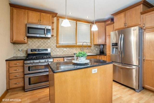 kitchen with dark stone countertops, light wood finished floors, a sink, stainless steel appliances, and a center island