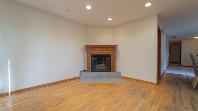 unfurnished living room featuring hardwood / wood-style floors, baseboards, a fireplace with raised hearth, and recessed lighting