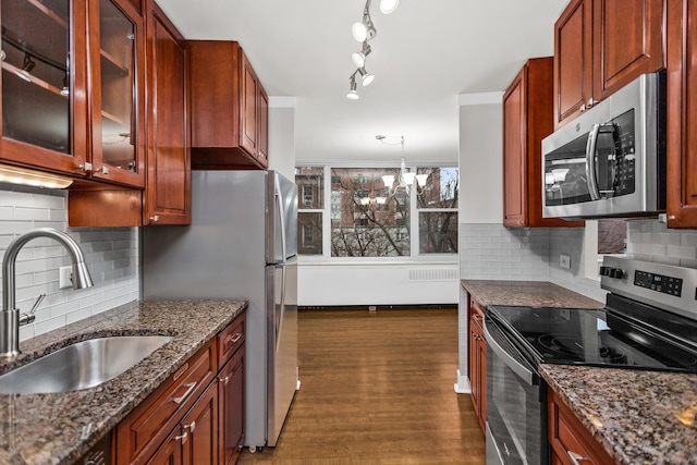 kitchen featuring dark wood-style flooring, dark stone countertops, appliances with stainless steel finishes, and a sink