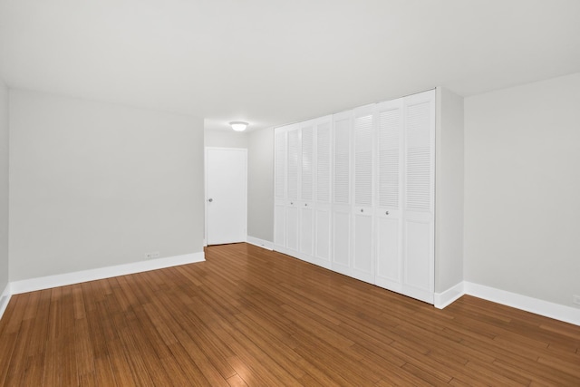 unfurnished bedroom featuring wood finished floors, baseboards, and a closet