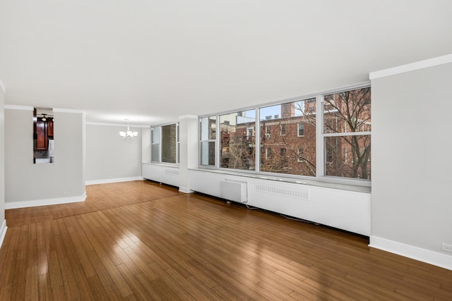 unfurnished living room featuring a notable chandelier, crown molding, and wood finished floors