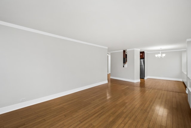 unfurnished living room with a chandelier, dark wood finished floors, crown molding, and baseboards