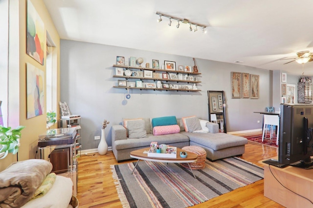 living area featuring baseboards, track lighting, wood finished floors, and a ceiling fan