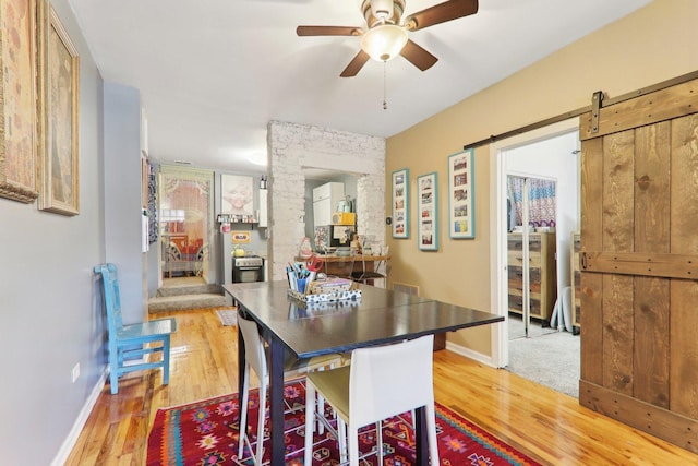 dining space featuring a barn door, baseboards, light wood finished floors, and ceiling fan